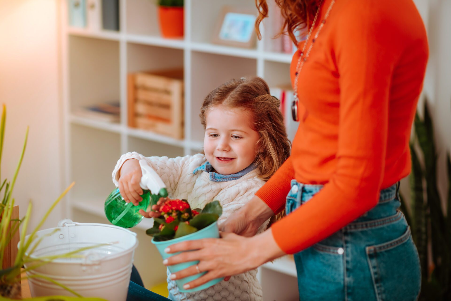 A mom and her child water a plant as they talk about what she did at the childcare center that day.
